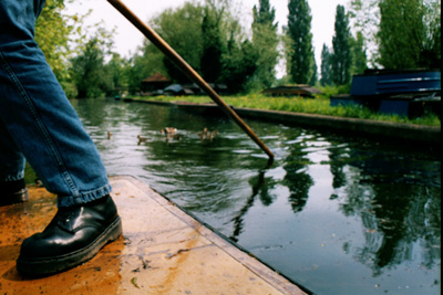 man standing on the back of a punt, pushing the pole into the river