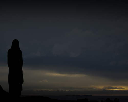 Dark image showing a woman silhouetted against a looming sky