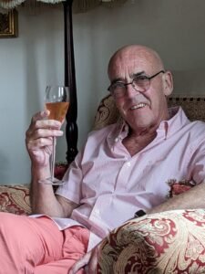 Robert sitting in an armchair raising a glass of pink champagne.